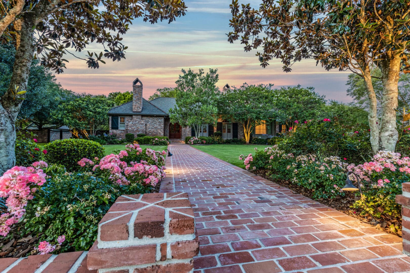 A brick walkway leading to a house with flowers in the foreground.