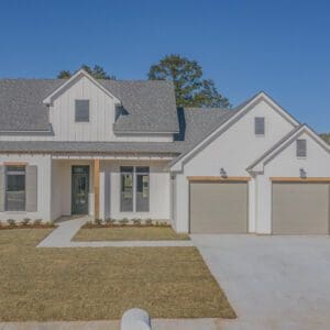 A white house with two garage doors and grass in front of it.