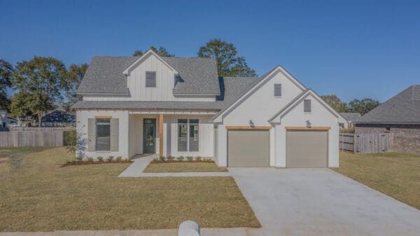 A white house with two garage doors and grass in front of it.