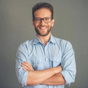 A man with glasses and beard standing in front of a gray wall.